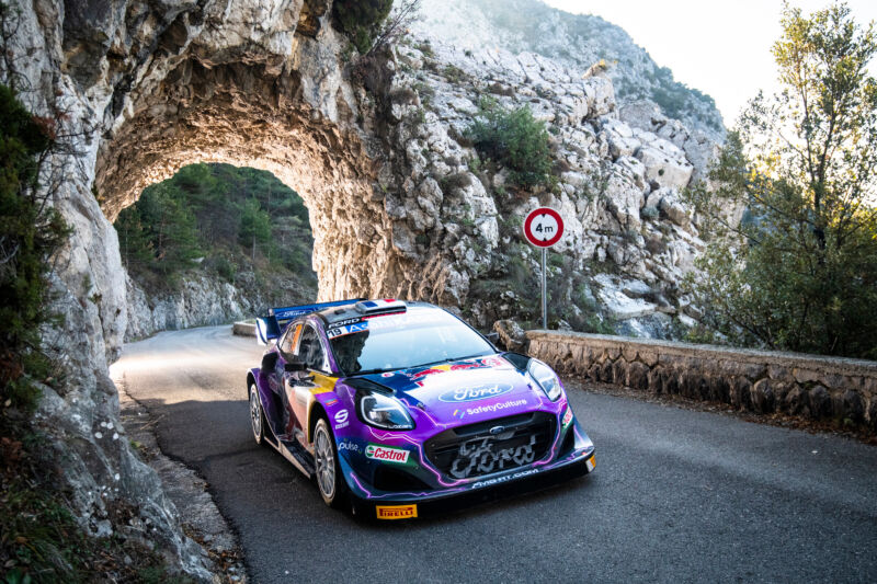 A brightly colored rally car drives through a rock tunnel