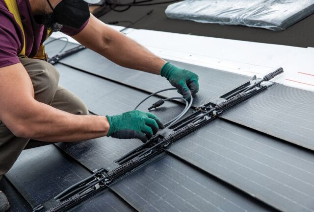 An installer makes electrical connections between rows of solar shingles.