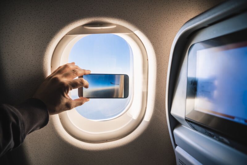 A person on an airplane using a smartphone to take a photo through the window.