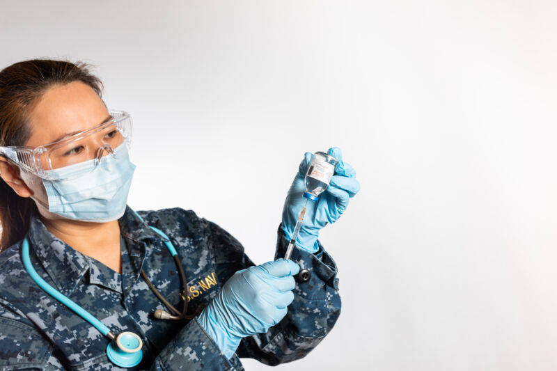 Nurse wearing a mask and Navy uniform prepares a vaccine.