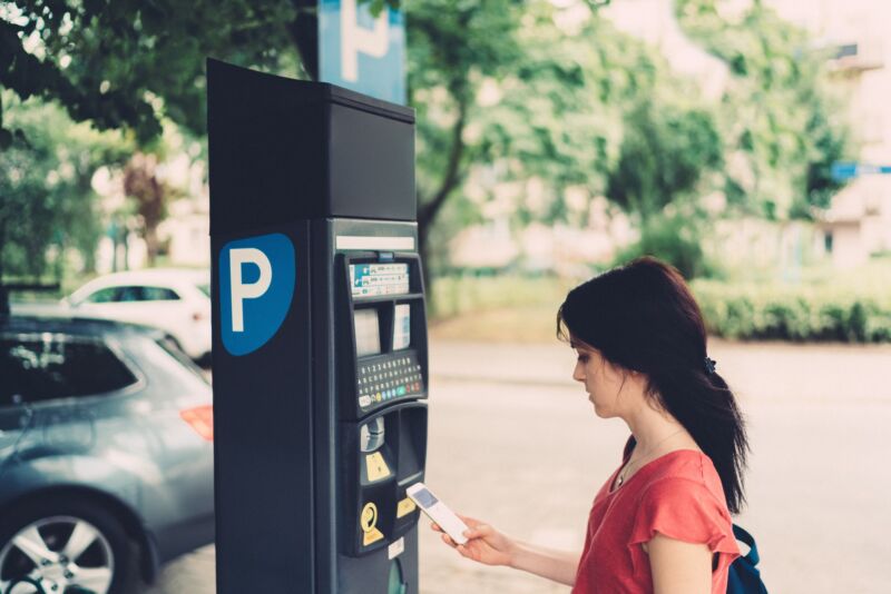 A woman paying for parking with a smartphone at a parking pay station.