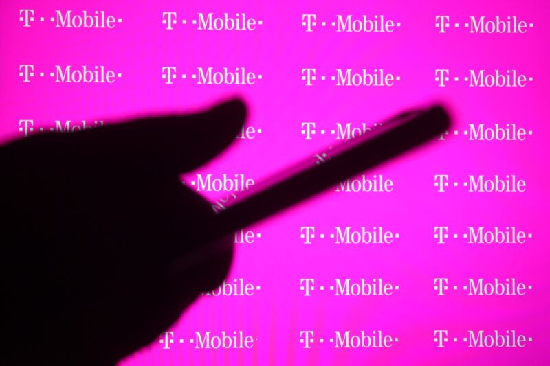 A person's hand holding a smartphone in front of a screen with T-Mobile logos.