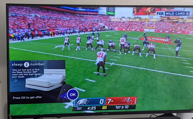 An ad appears over a sports game on a Sharp-branded TV running Roku software.