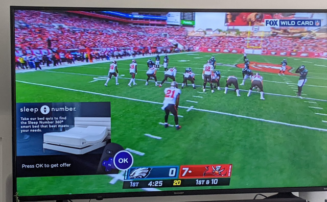 An ad appears over a sports game on a Sharp-branded TV running Roku software.