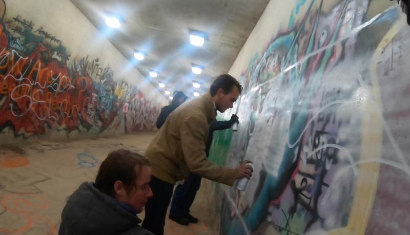 Men use spray paint to deface mural in public tunnel.