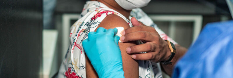 Image of a gloved hand holding a cotton ball to a person's arm.