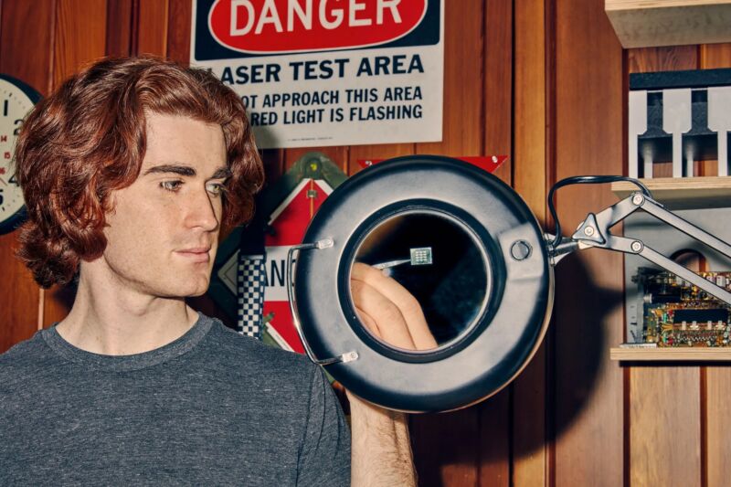 A young man with shaggy red hair holds up electronic components.