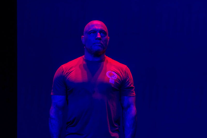 A buff guy in a tee-shirt is bathed in purple lighting.