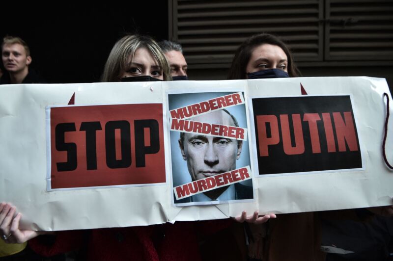 Protesters hold a sign with a picture of Russian President Vladimir Putin that says 