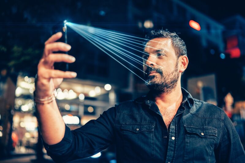 A man using a smartphone to take a selfie. The illustration has lines extending from the phone to his face to indicate that facial recognition is being used.