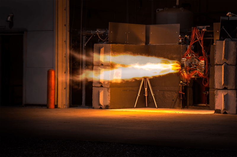 A rocket component belches flame in a darkened warehouse.