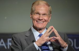 An older man in a suit smiles.