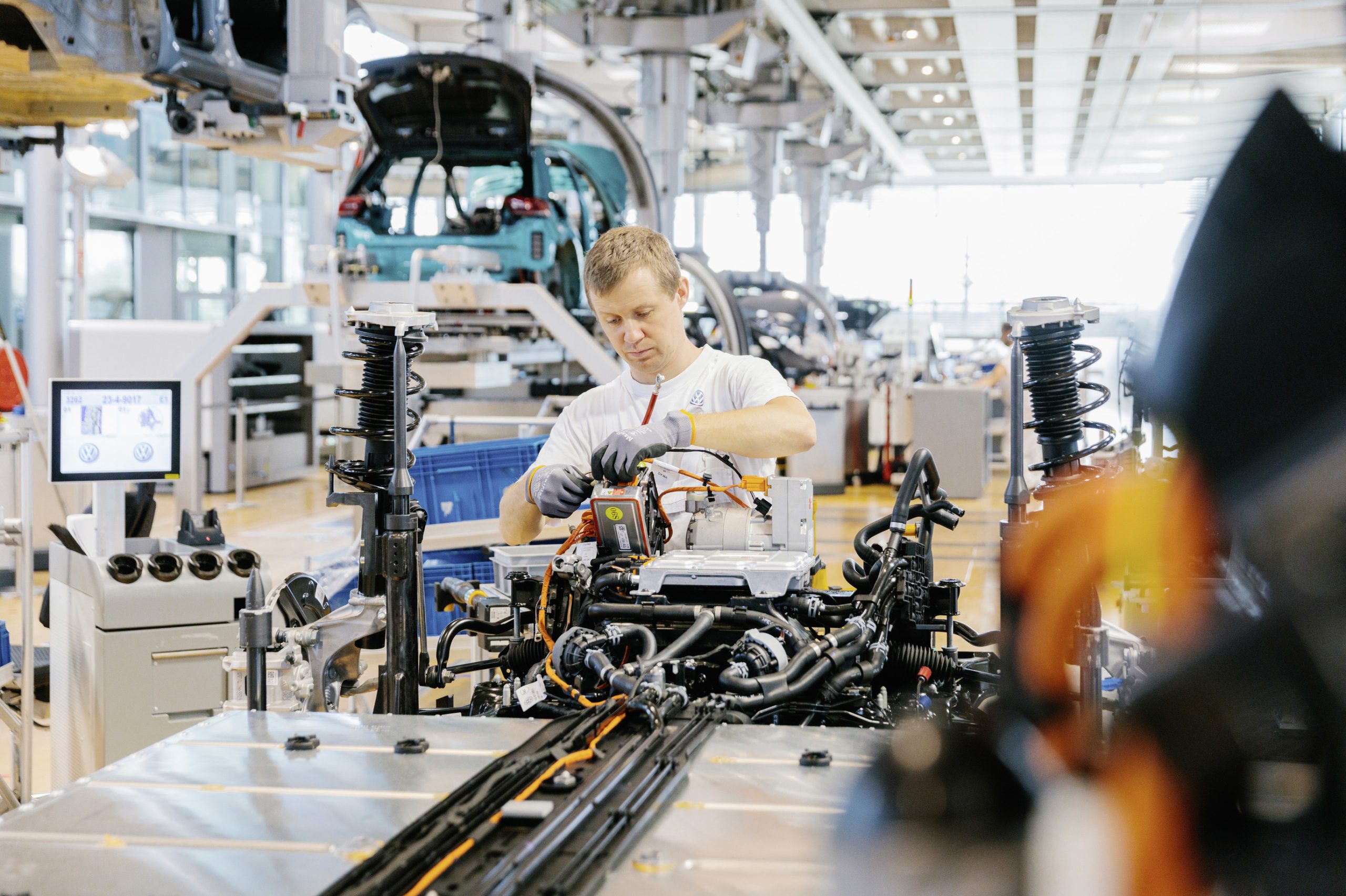 A gloved man works on a brightly lit, high-tech assembly line.