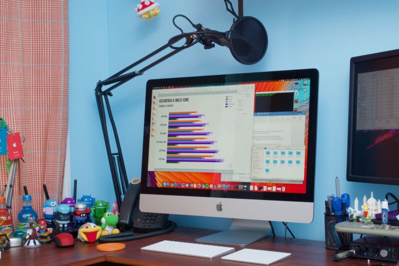 A large-screen computer sits atop a desk cluttered with pop-culture tchotchkes.