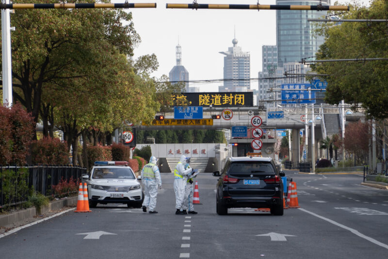 Medical workers in hazmat suits talk to a stopped driver.