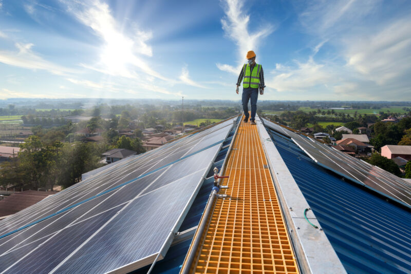 Image of a workman on top of a roof covered in solar panels.
