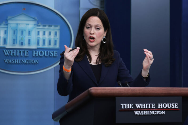 A smartly dressed woman gesticulates while speaking from a podium.