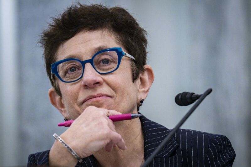 Gigi Sohn sits in front of a microphone and holds a pen in her hand at a Senate nomination hearing.