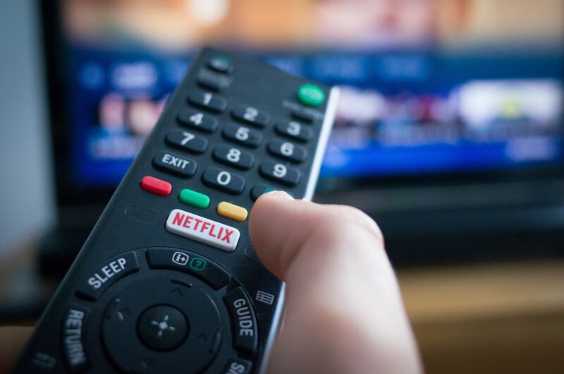 A person's hand holding a TV remote control with a Netflix button.