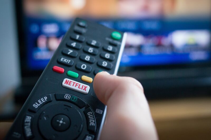 A person's hand holding a TV remote with a Netflix button.