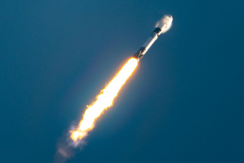 A rocket leaves a trail of fire as it roars across a blue sky.