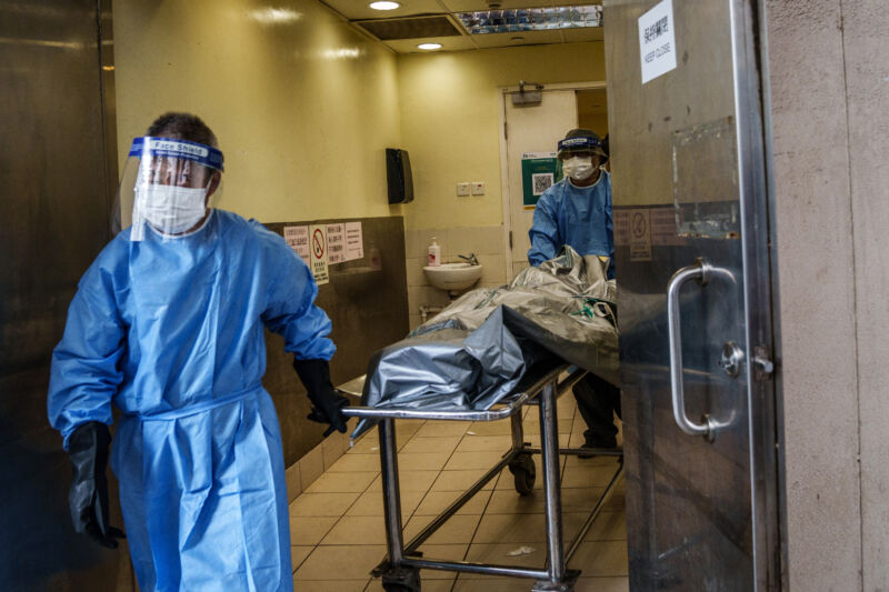 Health care workers wearing personal protective equipment transport the body of a deceased patient onto a hearse outside the mortuary at the Queen Elizabeth Hospital in Hong Kong, China, on Wednesday, March 2, 2022. Hong Kong reported more than 55,000 cases on Wednesday, its hospitals are inundated, and the city's morgues are nearly full.