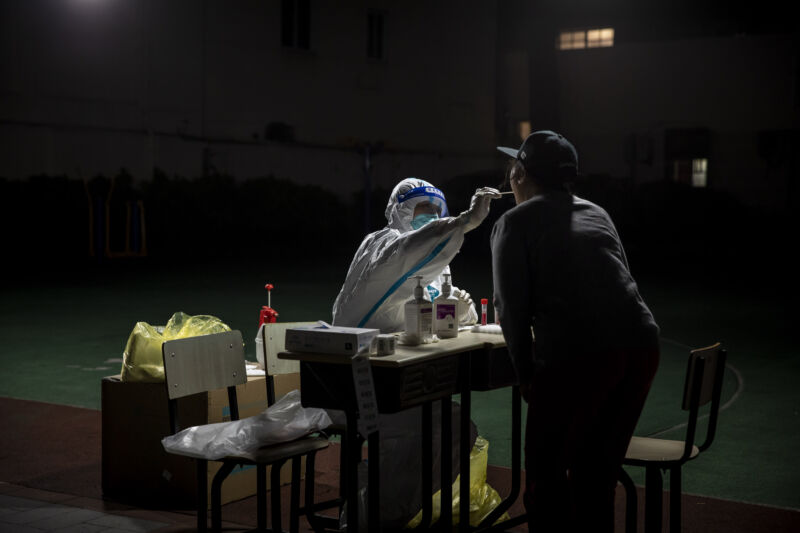A worker in personal protective equipment (PPE) collects a swab sample from a resident for a COVID-19 test in a neighborhood placed under lockdown in Shanghai, China, on Saturday, April 9, 2022. 
