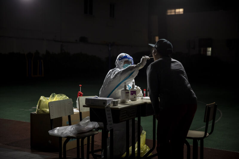 A worker in personal protective equipment (PPE) collects a swab sample from a resident for a COVID-19 test in a neighborhood placed under lockdown in Shanghai, China, on Saturday, April 9, 2022.