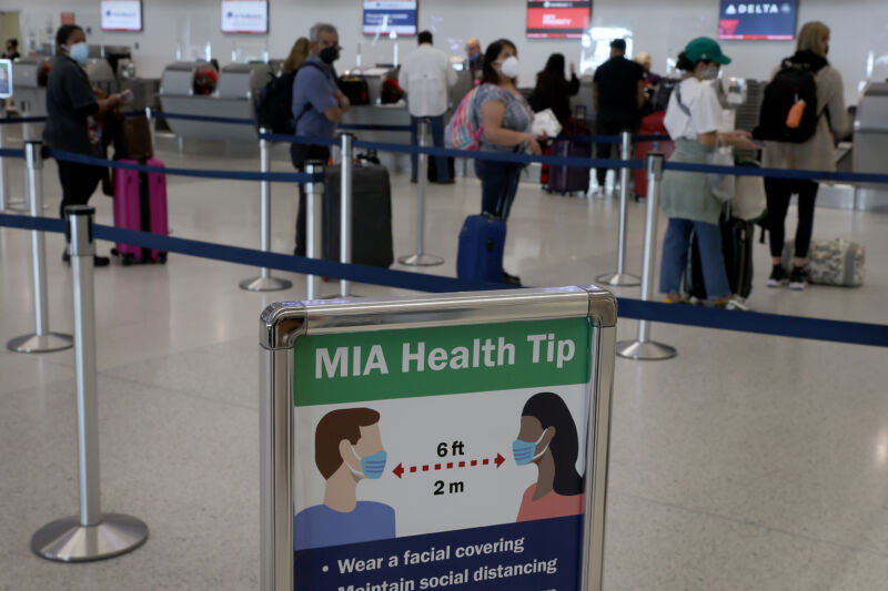 A sign advises people to wear a mask and stand six feet apart as travelers make their way through Miami International Airport on December 28, 2021.