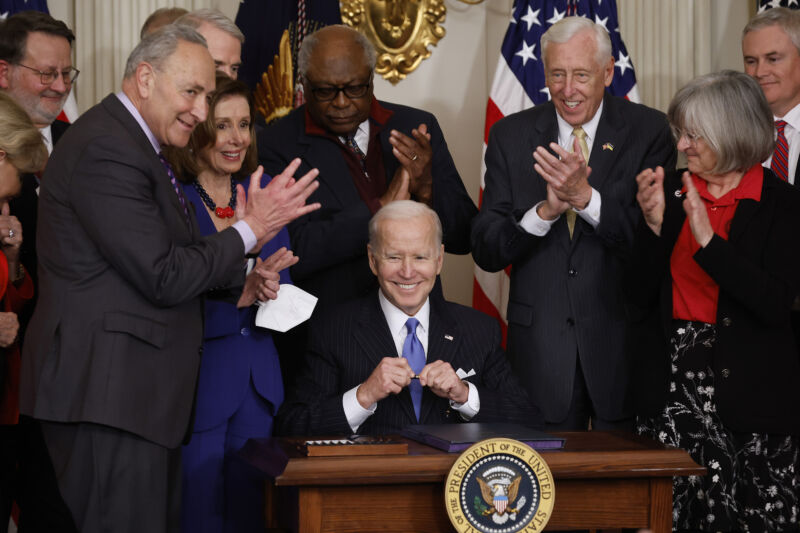 US President Joe Biden (C) signs the Postal Service Reform Act into law during an event with (L-R) Sen. Gary Peters (D-Mich.), Senate Majority Leader Charles Schumer (D-N.Y.), Speaker of the House Nancy Pelosi (D-Calif.), House Majority Whip James Clyburn (D-S.C.), House Majority Leader Steny Hoyer (D-Md.) and retired letter carrier Annette Taylor and others in the State Dining Room at the White House on April 6, 2022 in Washington, DC.
