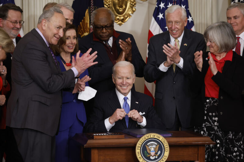 US President Joe Biden (C) signs the Postal Service Reform Act into law during an event with (L-R) Sen. Gary Peters (D-Mich.), Senate Majority Leader Charles Schumer (D-N.Y.), Speaker of the House Nancy Pelosi (D-Calif.), House Majority Whip James Clyburn (D-S.C.), House Majority Leader Steny Hoyer (D-Md.) and retired letter carrier Annette Taylor and others in the State Dining Room at the White House on April 6, 2022 in Washington, DC. 