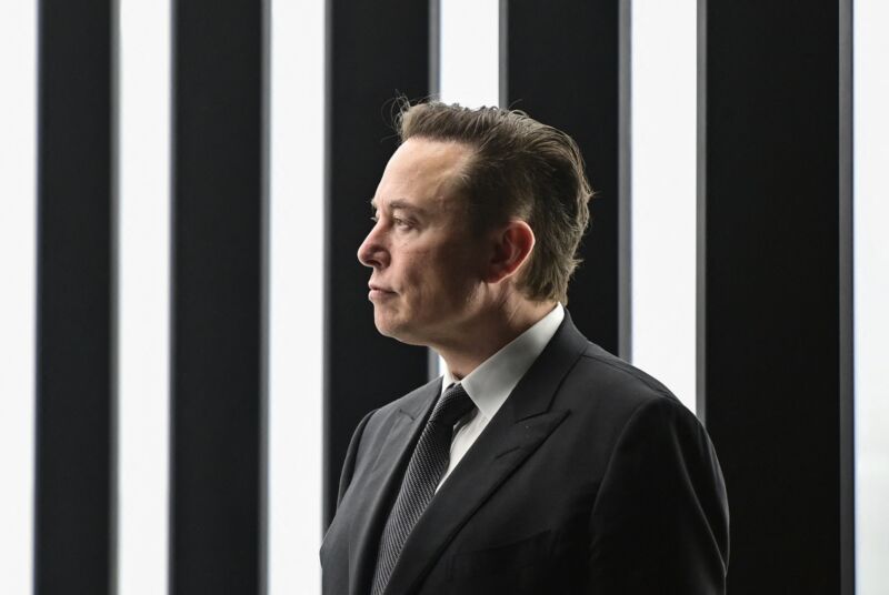 Elon Musk wearing a suit during an event at a Tesla factory.