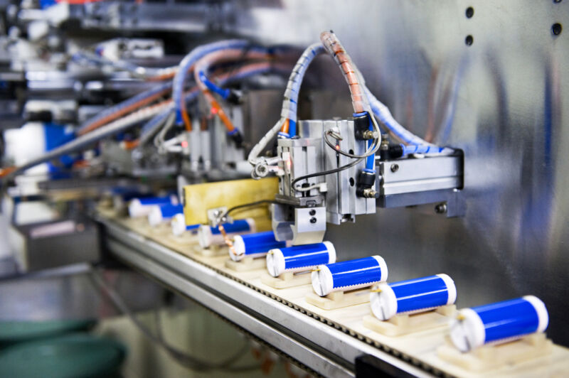 Image of blue cylinders on a track that passes beneath industrial equipment.