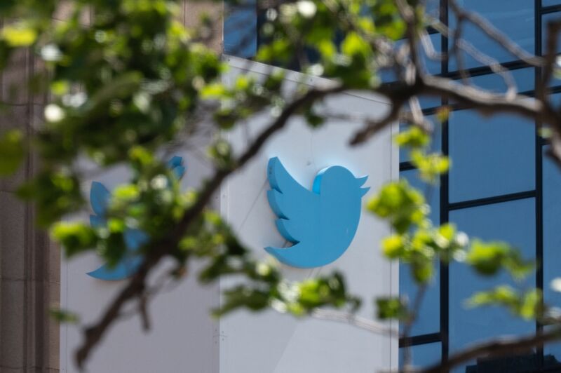 Twitter's bird-shaped logo on the outside of the company's headquarter building. The camera angle also shows nearby tree branches, making it appear as if the bird is sitting on a branch or flying through the branches.