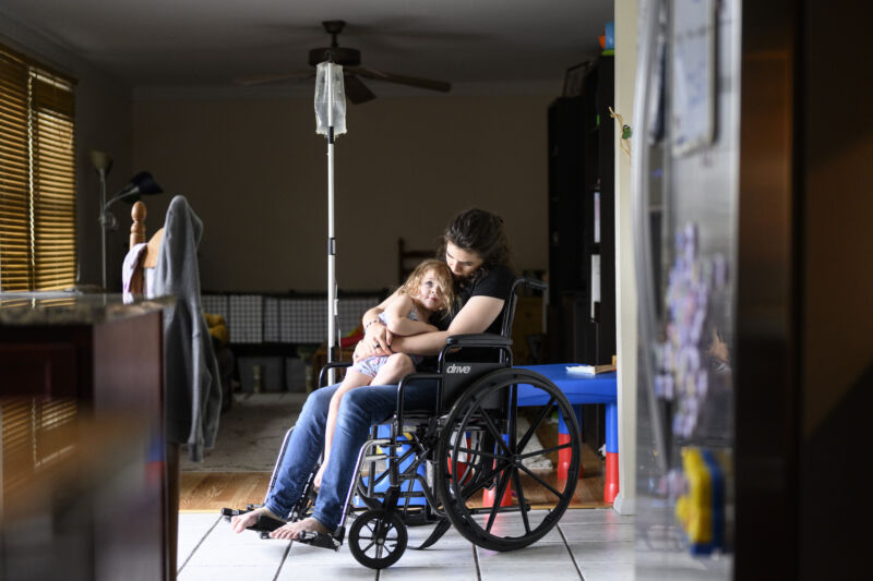 Seorang pasien COVID panjang duduk dengan putrinya di kursi rodanya saat menerima infus saline di rumahnya di Maryland pada Jumat, 27 Mei 2022.  