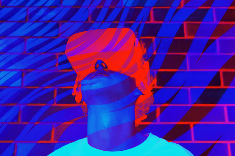 Jeune homme ou adolescent dans un t-shirt blanc portant un casque de réalité virtuelle pendant l'expérience VR dans les couleurs néon ultra violet violet et bleu fluorescent.