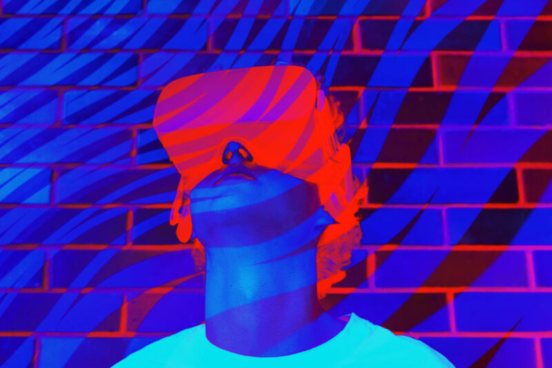 Joven o adolescente con una camiseta blanca con auriculares de realidad virtual durante la experiencia de realidad virtual en colores púrpura y azul ultravioleta fluorescente neón.