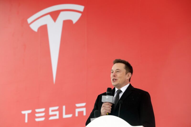 Tesla CEO Elon Musk holds a microphone and speaks at an event at a factory in China.