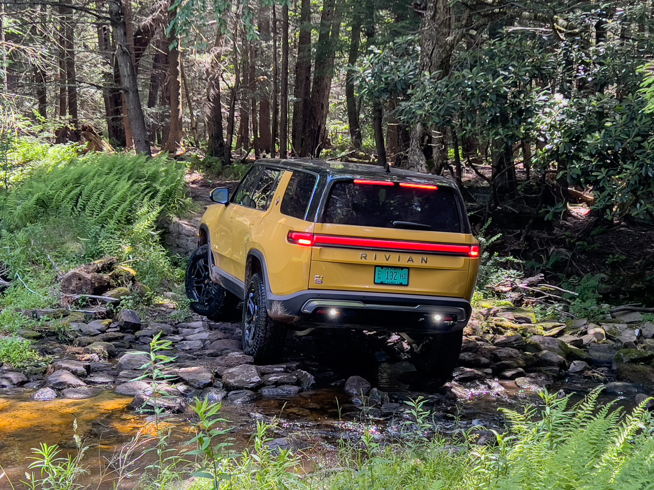 A yellow Rivian R1T driving off road, seen from behind,