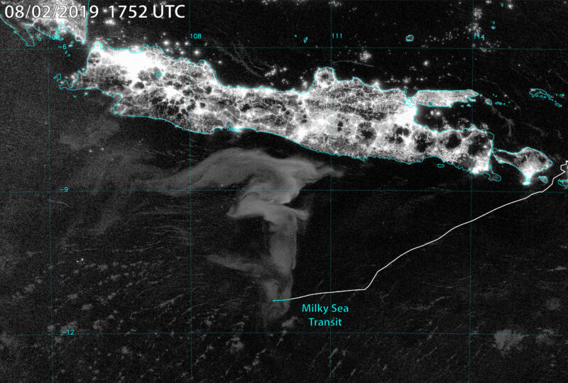 The black-and-white satellite image shows an island covered in intense lighting just north of a dimly lit ocean whirlpool.