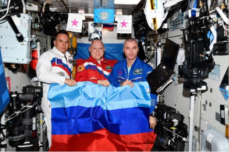 Cosmonauts Oleg Artemyev, Denis Matveyev, and Sergey Korsakov pose with a flag of the Luhansk People's Republic on the International Space Station.