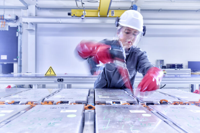 A woman wearing a hardhat and anti-shock gloves dismantles a battery pack