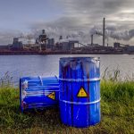 Image of waste drums and an industrial facility next to a river.