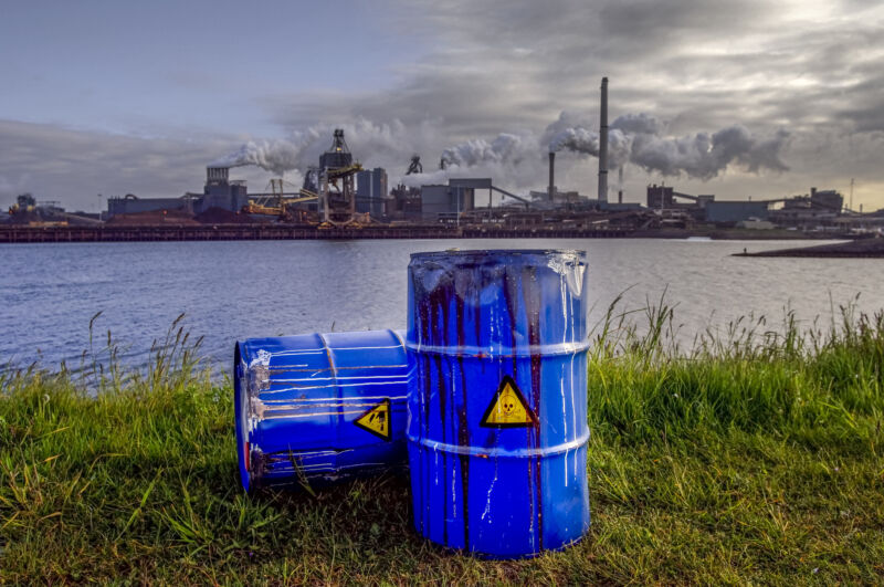 Image of waste drums and an industrial facility next to a river.