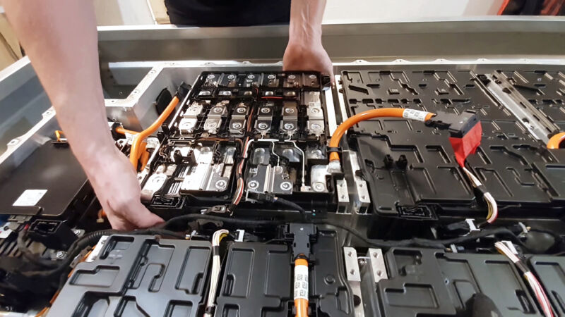close-up of a mechanic's hands disassembling an electric car battery on top of a trailer inside a mechanic shop