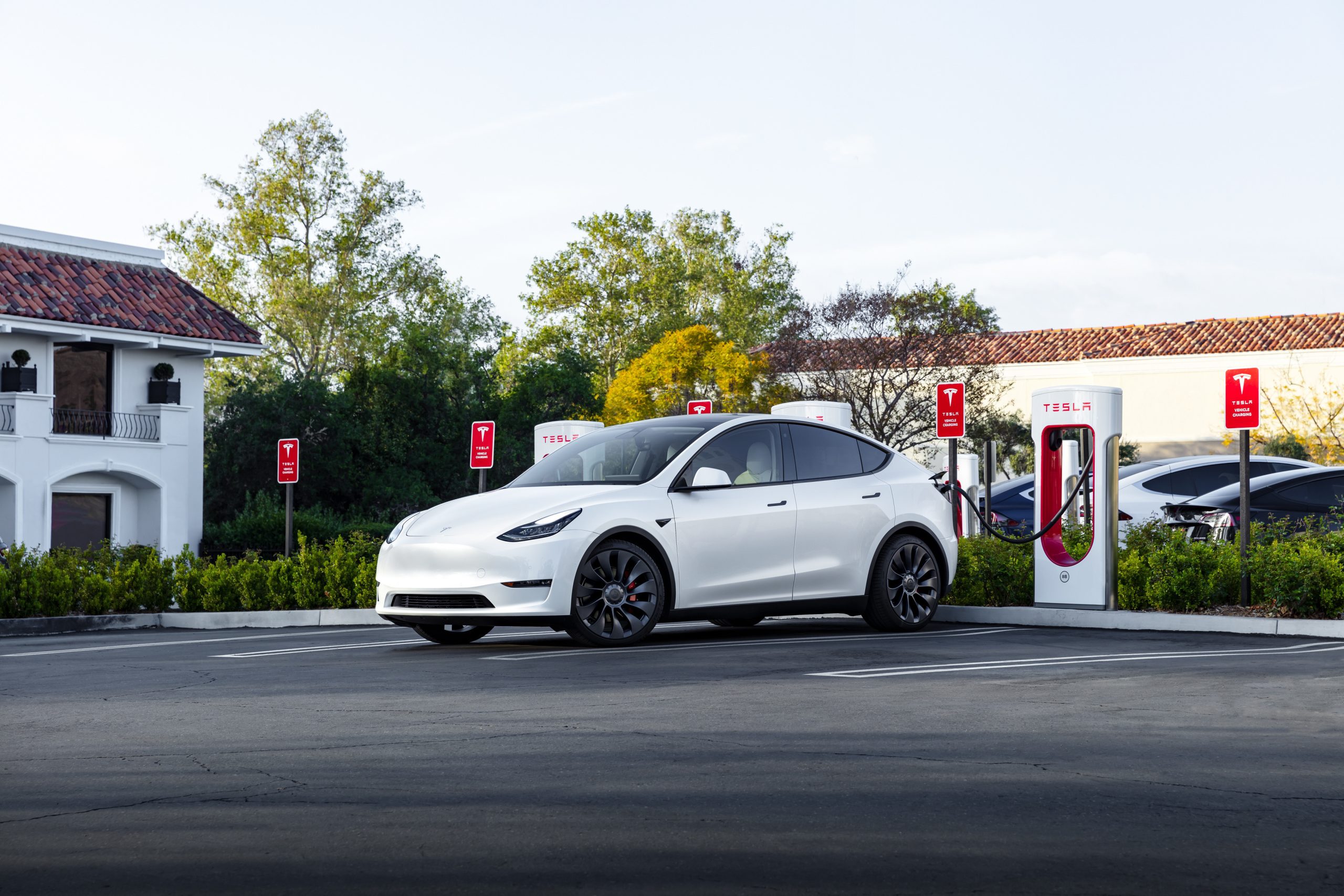 A white Tesla Model Y at a supercharger