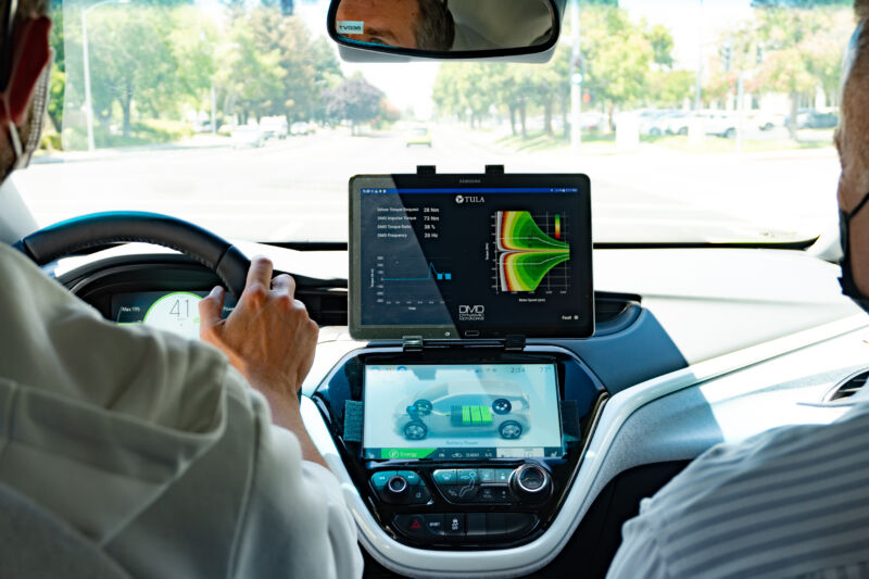 An iPad is mounted to the dash of a Chevrolet Bolt. Two men are in the front seats, each wearing a face mask.