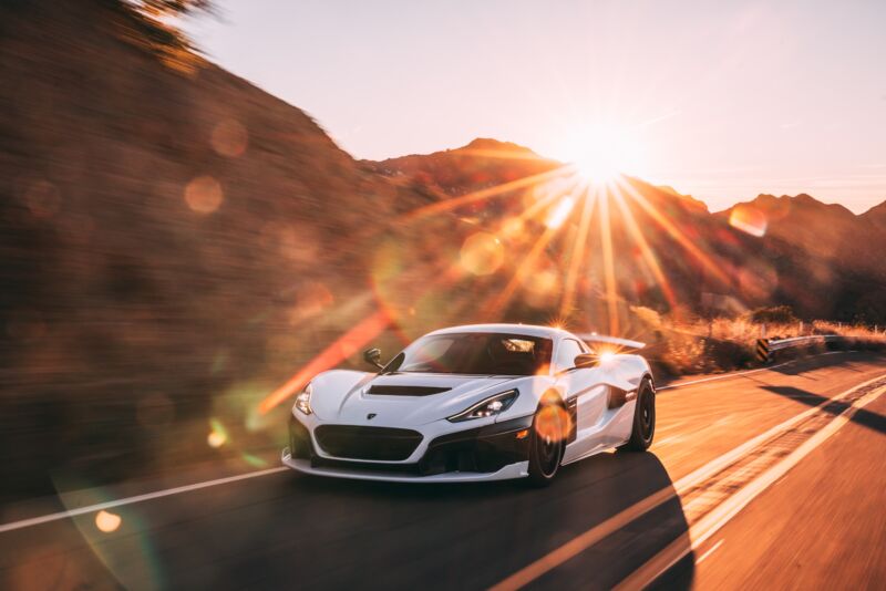 A white Rimac Nevera with the sun bursting over a mountain in the background