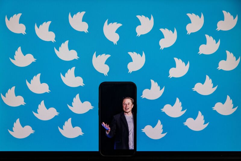 A cell phone displaying a photo of Elon Musk placed on a computer screen filled with Twitter logos.