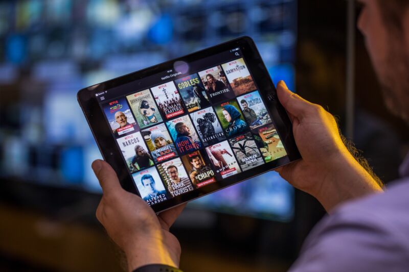 Un hombre con un iPad que muestra una lista de programas disponibles en Netflix.